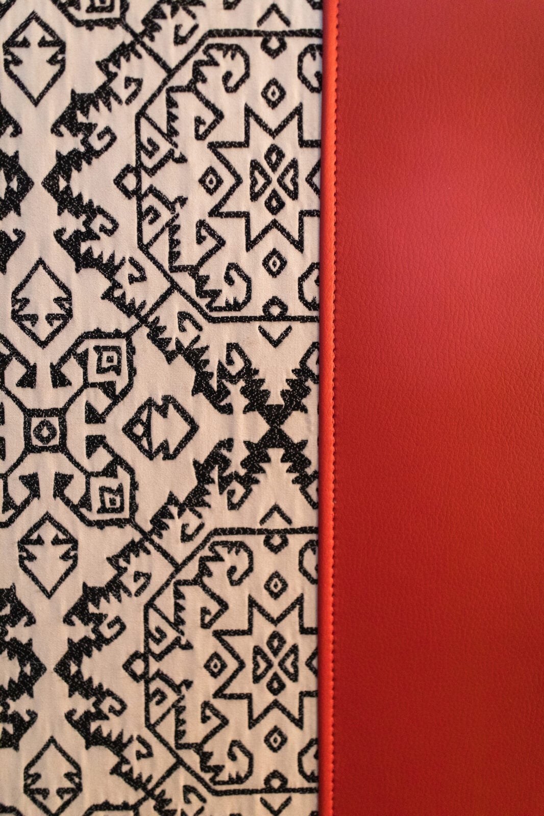 Black geometric pattern on white fabric next to a vertical strip of textured red material, with a visible seam between the two surfaces.