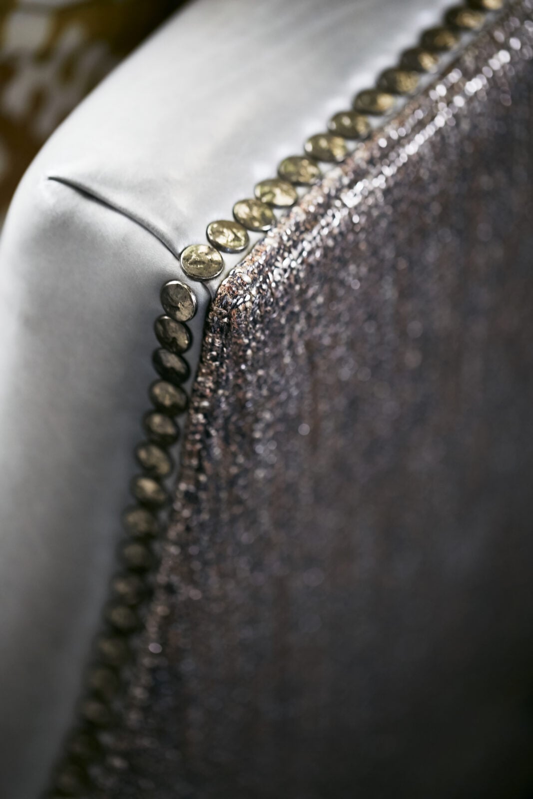 Close-up of a chair’s textured fabric and smooth upholstery, featuring a row of decorative metallic studs along the edge.