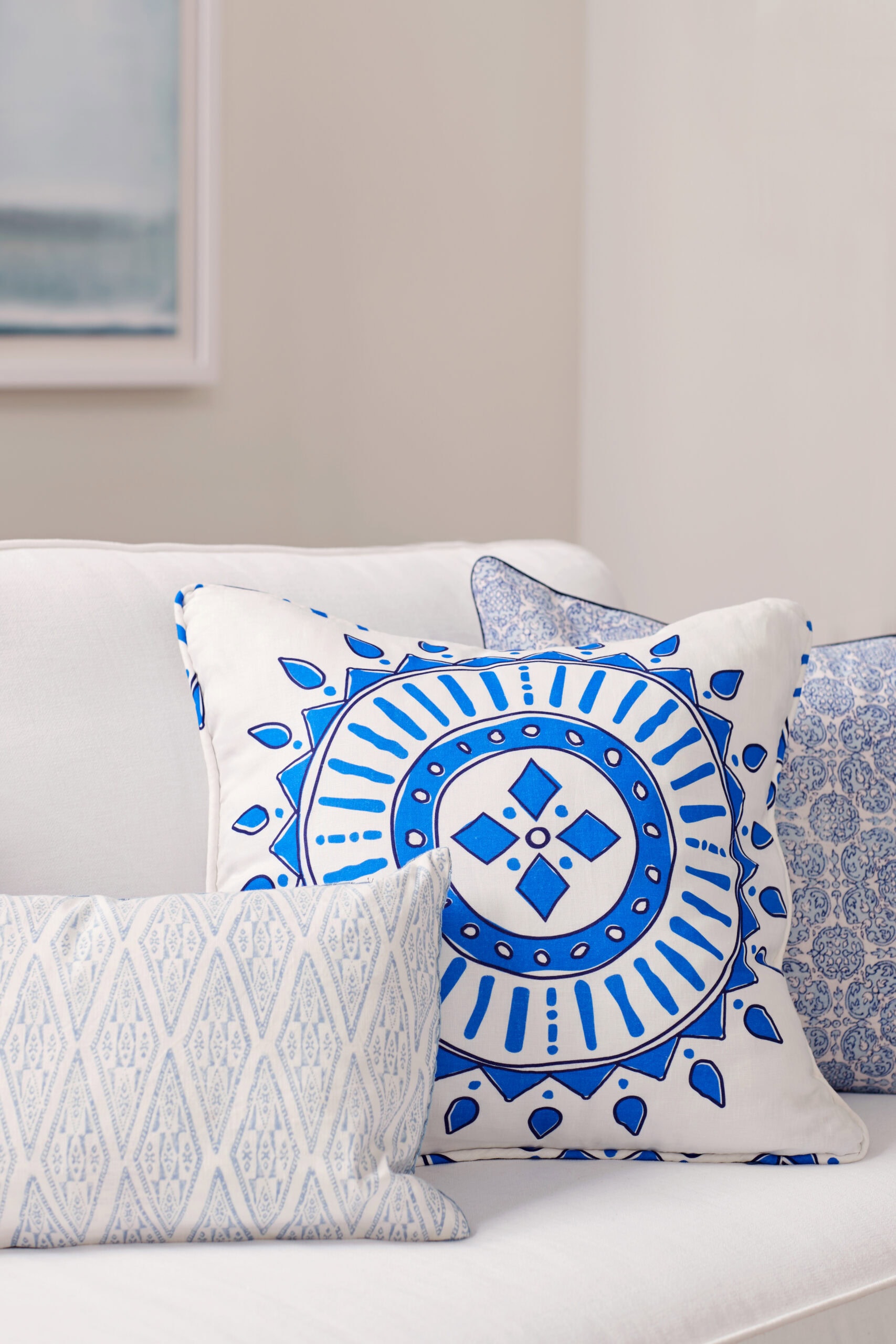 White sofa with three decorative throw pillows; the front pillow has a bold blue and white geometric pattern, while the others have subtle blue designs.