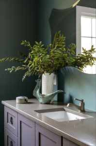 Green bathroom with a white potted plant on the counter and additional blue and white accessories on the bathroom vanity