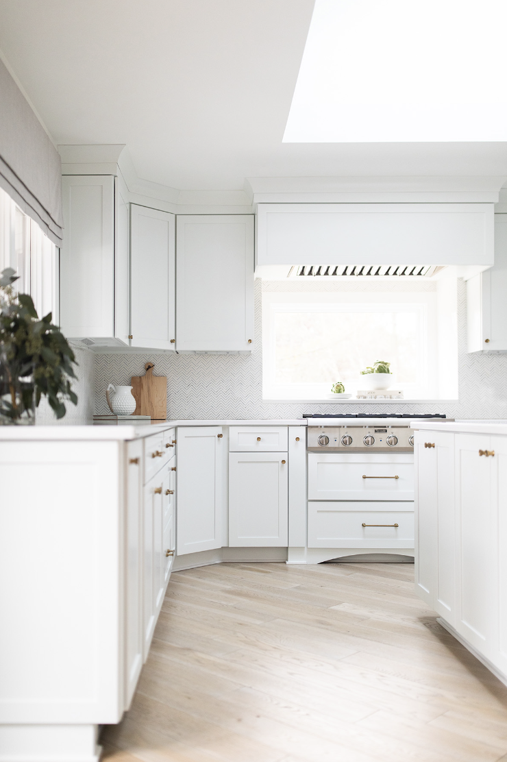 Image of white updated, modern kitchen. All white cabinets, skylight above, white oak flooring