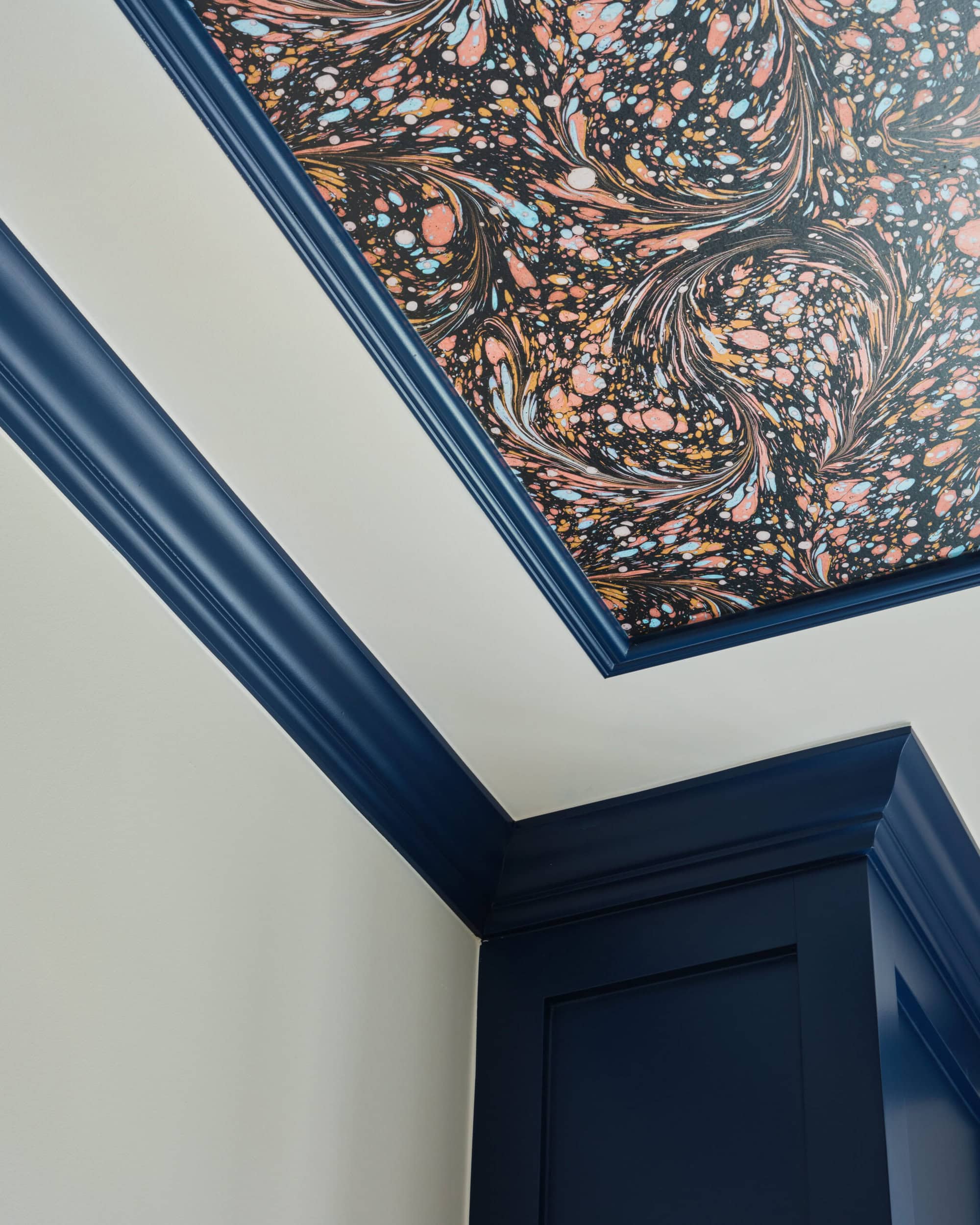 A ceiling corner with dark blue crown molding and a colorful, marbled patterned wallpaper on the ceiling.