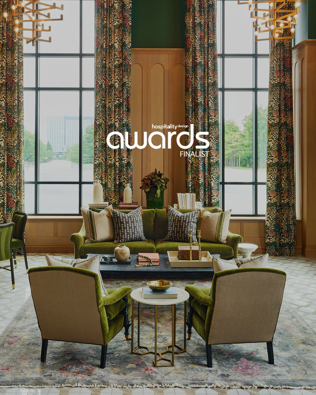 Elegant hotel lobby with tall floral curtains, green velvet sofa, beige armchairs, coffee table, and large windows; text reads "Hospitality Design Awards Finalist.