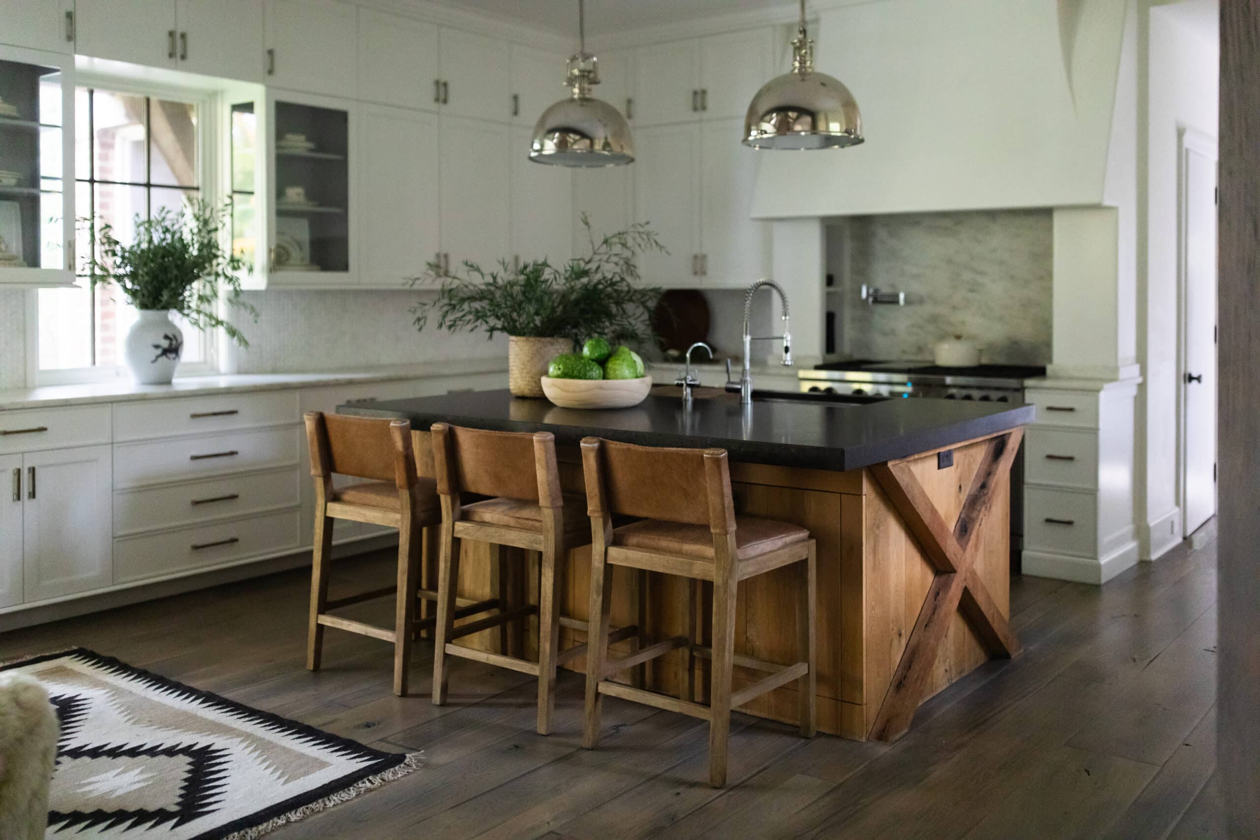 Modern kitchen with white cabinets, a wood island with black countertop, three wooden bar stools, pendant lights, and greenery decor on the island and counter.