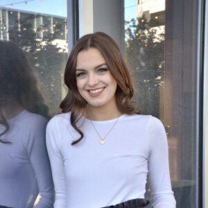 Girl in front of reflective window in industrial building wearing a white long sleeve shirt and black leather pants