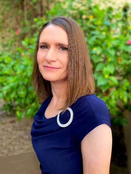 Woman with short brown hair wearing a royal blue shirt standing in front of a wall of ivy