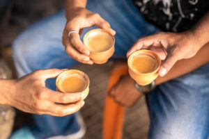 Three hands holding cups of tea together in a circle sitting in orange chairs and wearing blue jeans