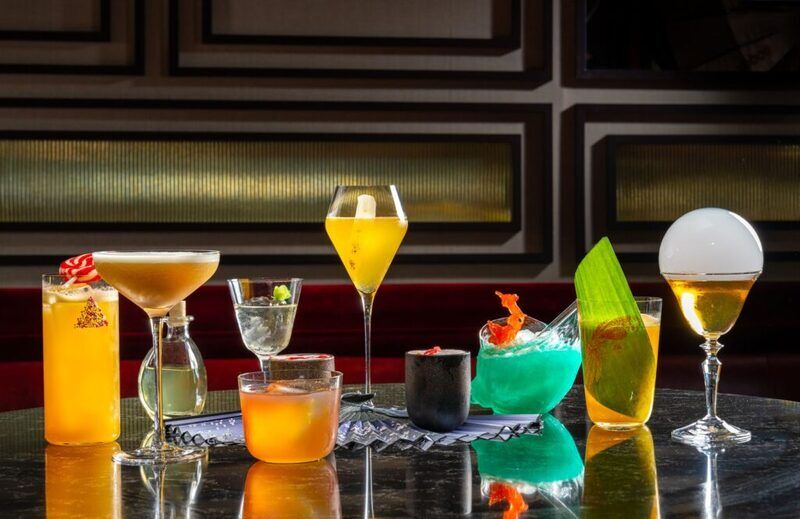 ten various cocktails on a shinny reflective dark brown counter top with a wood molding accent wall background