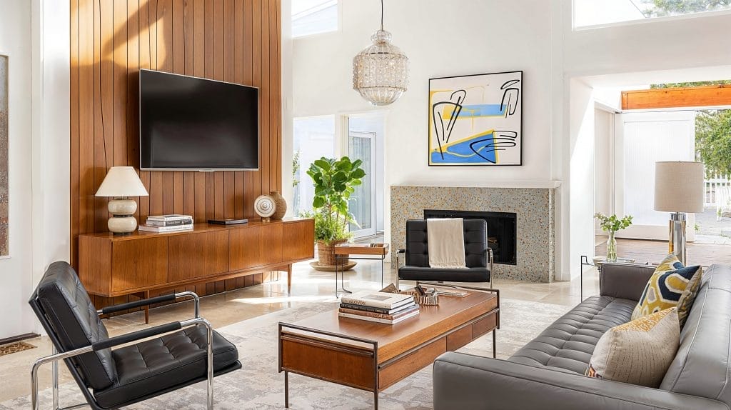 Design room with a wood panel fireplace with a television above it and a wooden coffee table with grey lounge seating and pop art