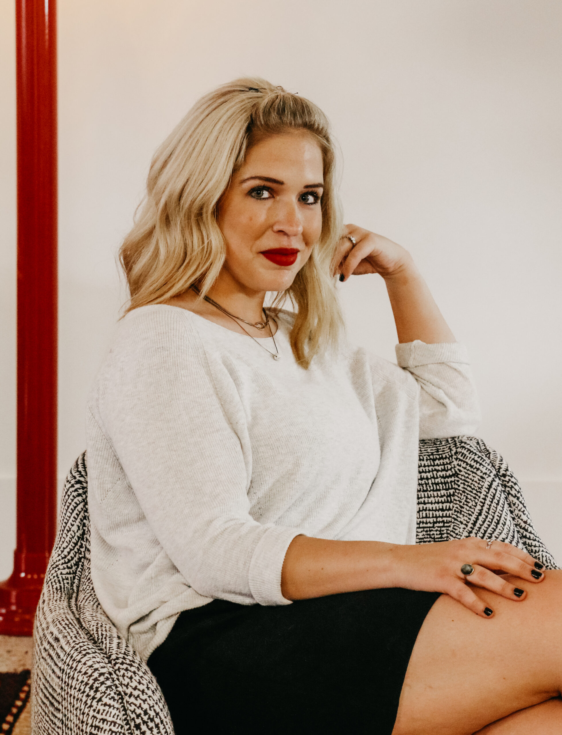 A caucasian woman with blonde hair wearing a white blouse and black skirt sitting in a grey upholstered lounge chair
