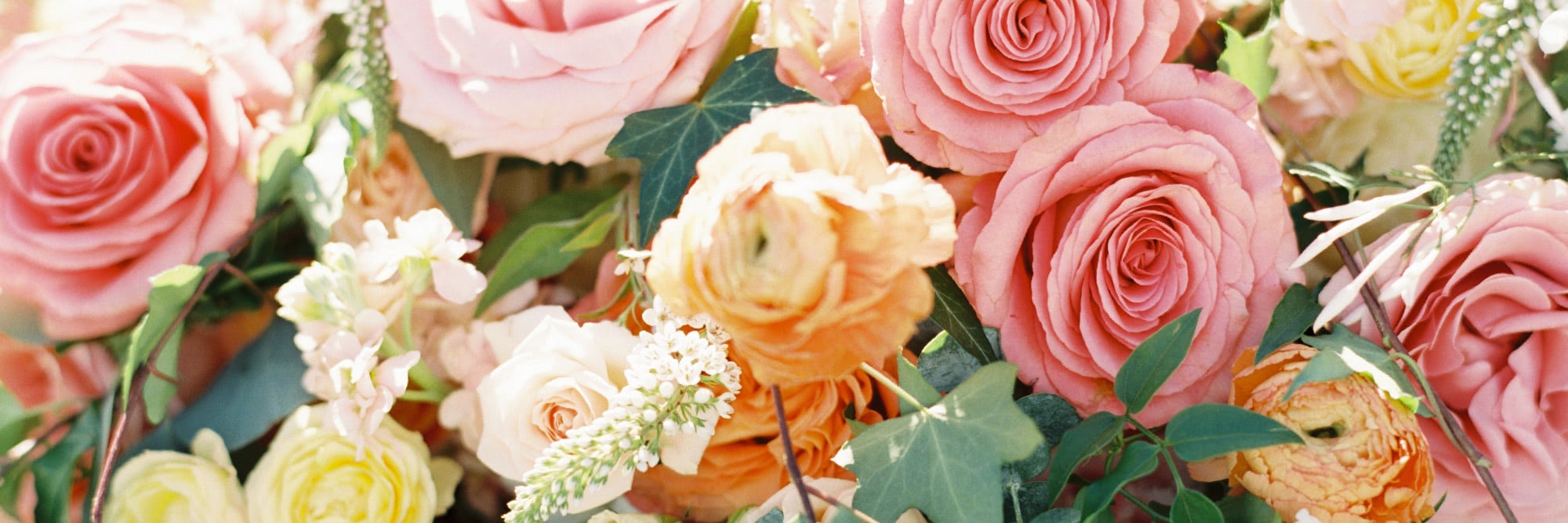 Arrangement of mixed florals including pink roses, peach colored roses, white baby's breath flowers, and ivy leaves