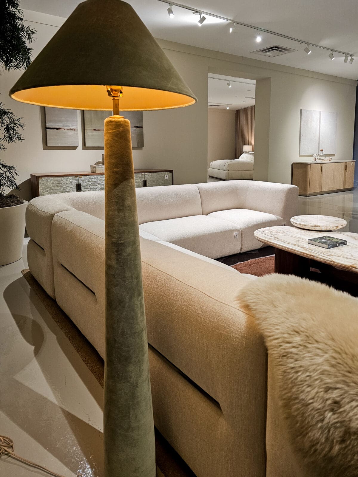 A modern living room with a large beige sectional sofa, marble coffee table, floor lamp, wall art, and neutral decor.