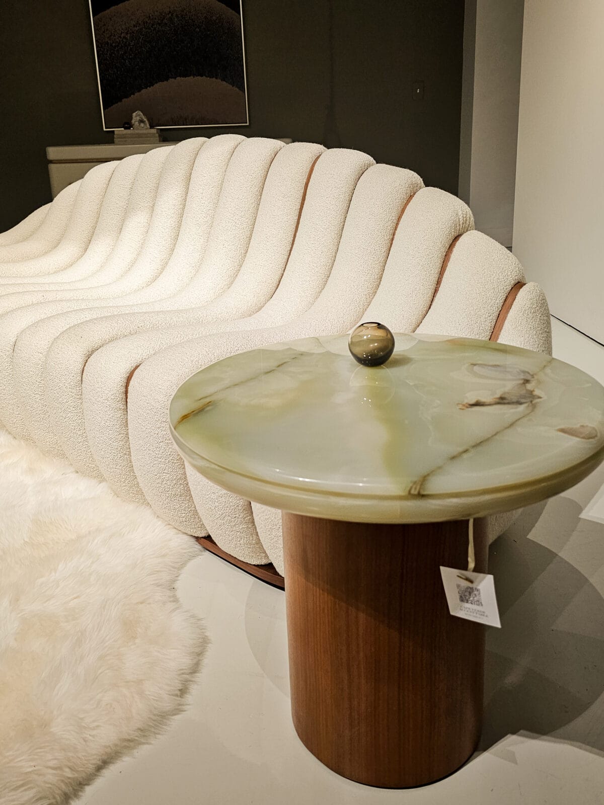 Curved, textured cream sofa next to a round marble-top side table with a brown base, in a modern, minimal living space.