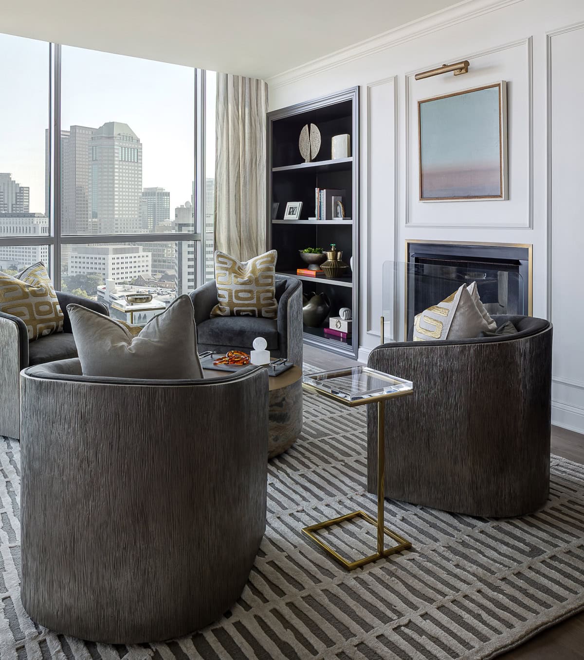 Modern living room with two grey swivel chairs, a glass side table, built-in shelves, a fireplace, and large windows overlooking a cityscape.