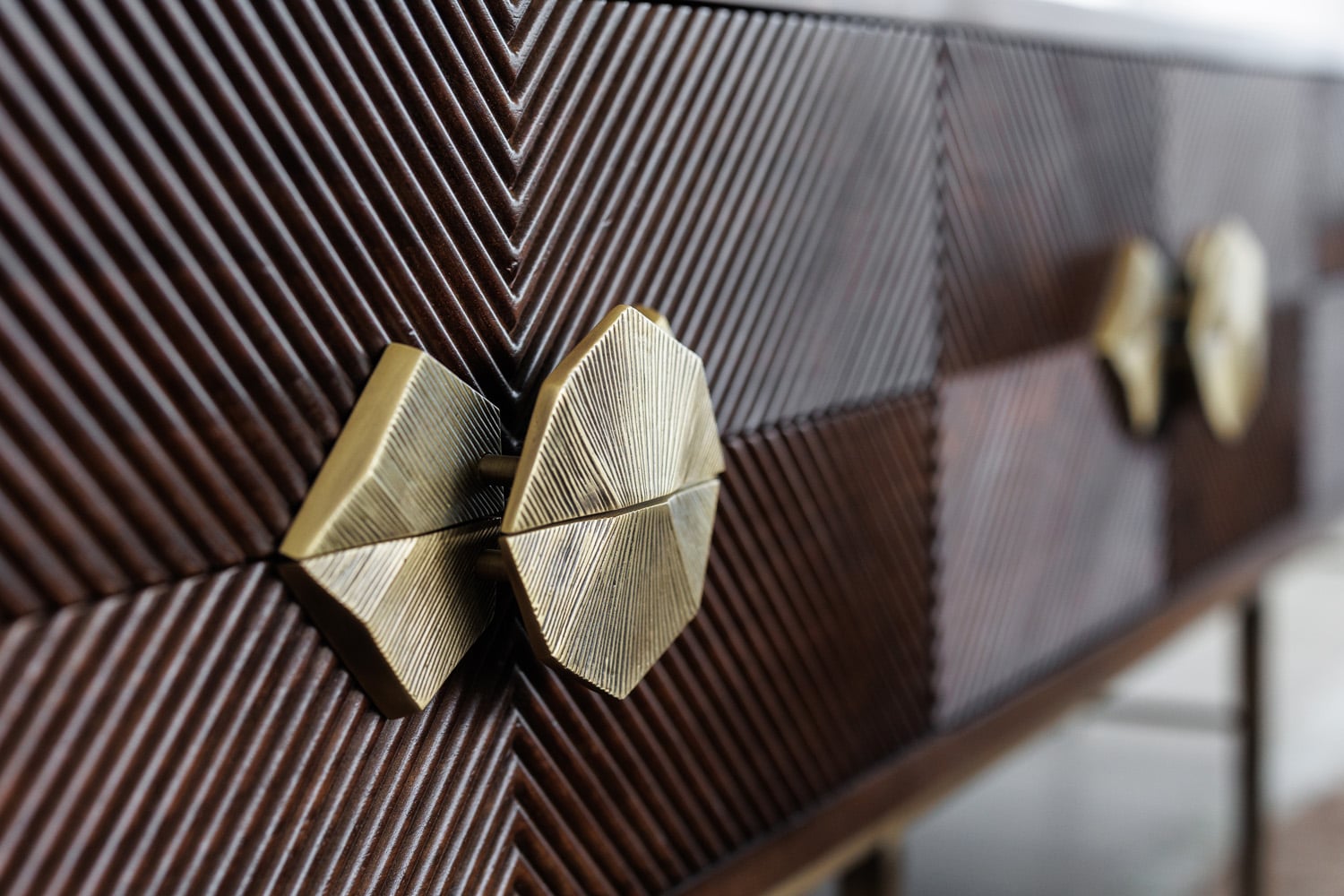 Close-up of a dark wood dresser with a chevron pattern and geometric gold drawer handles.