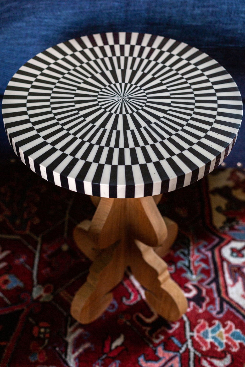 A small round table with a black and white geometric pattern top, wooden pedestal base, placed on a patterned rug.