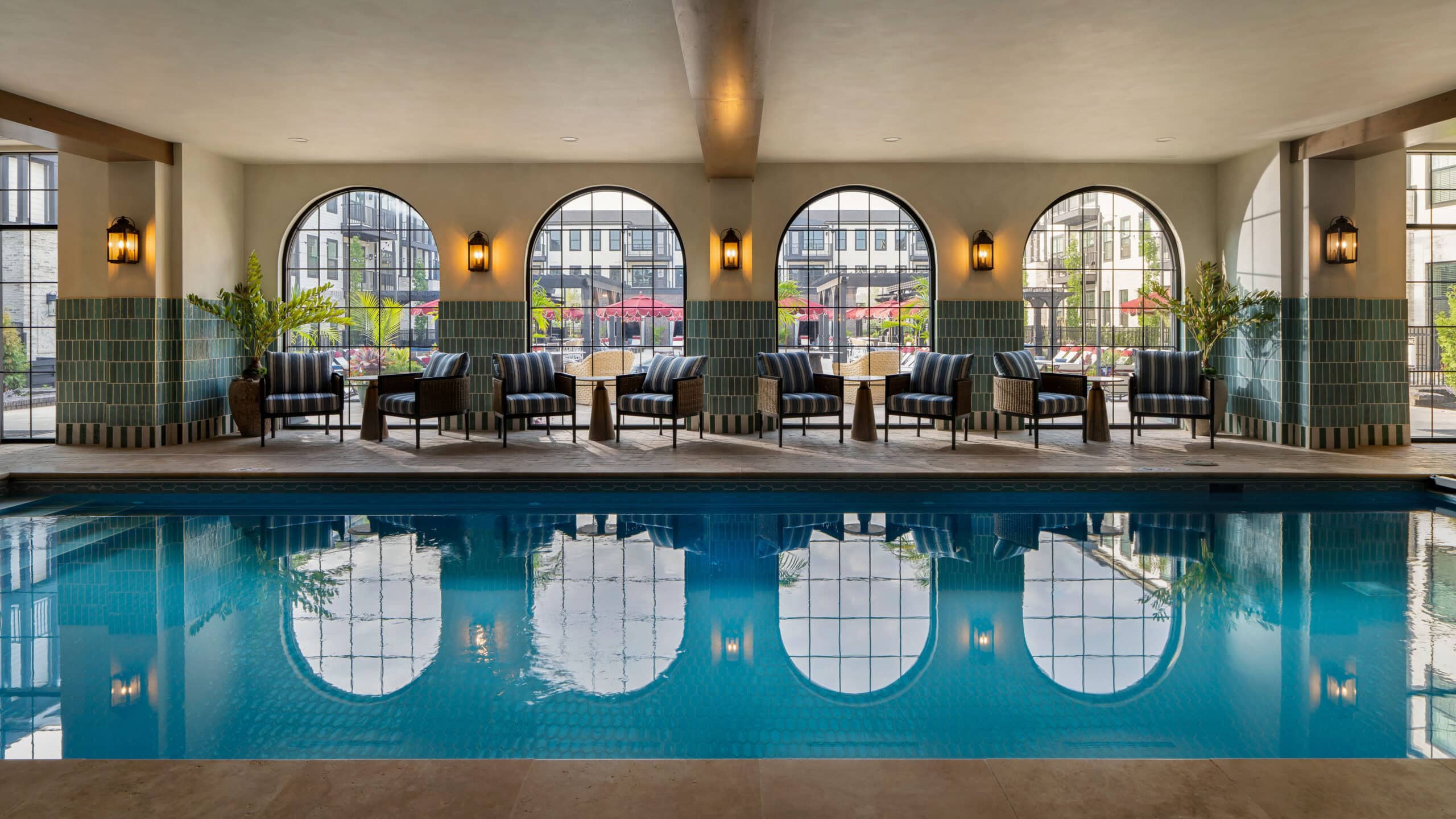 Indoor pool with clear water, lounge chairs, and tables in front of large arched windows overlooking an outdoor patio area—a perfect example of refined leisure spaces inspired by retail design in Scottsdale, Arizona.