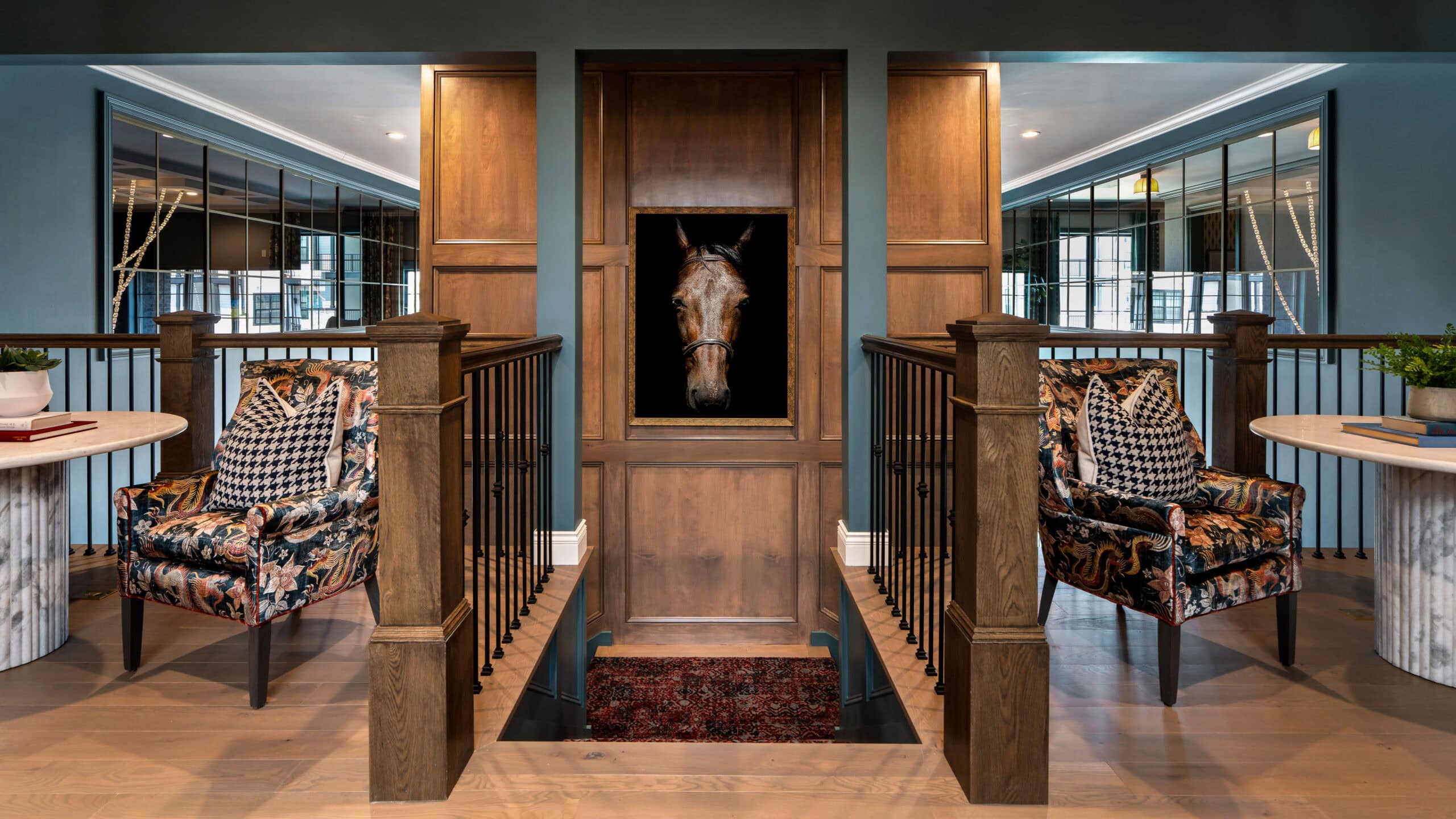 Two patterned armchairs face each other in a hallway with wood paneling, flanked by mirrors and side tables, and a framed horse portrait in the center background above a staircase—an inviting arrangement that exemplifies sophisticated retail design in Scottsdale, Arizona.