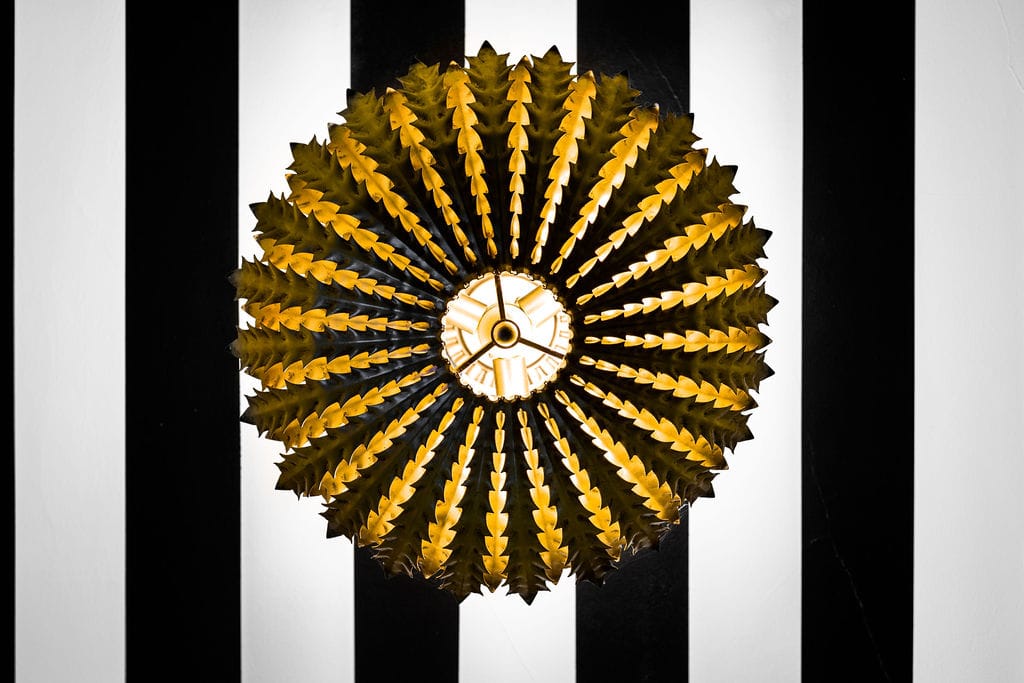 A luxury sunburst-style gold wall sconce mounted on a modern black and white striped architectural wall panel for a boutique commercial interior.