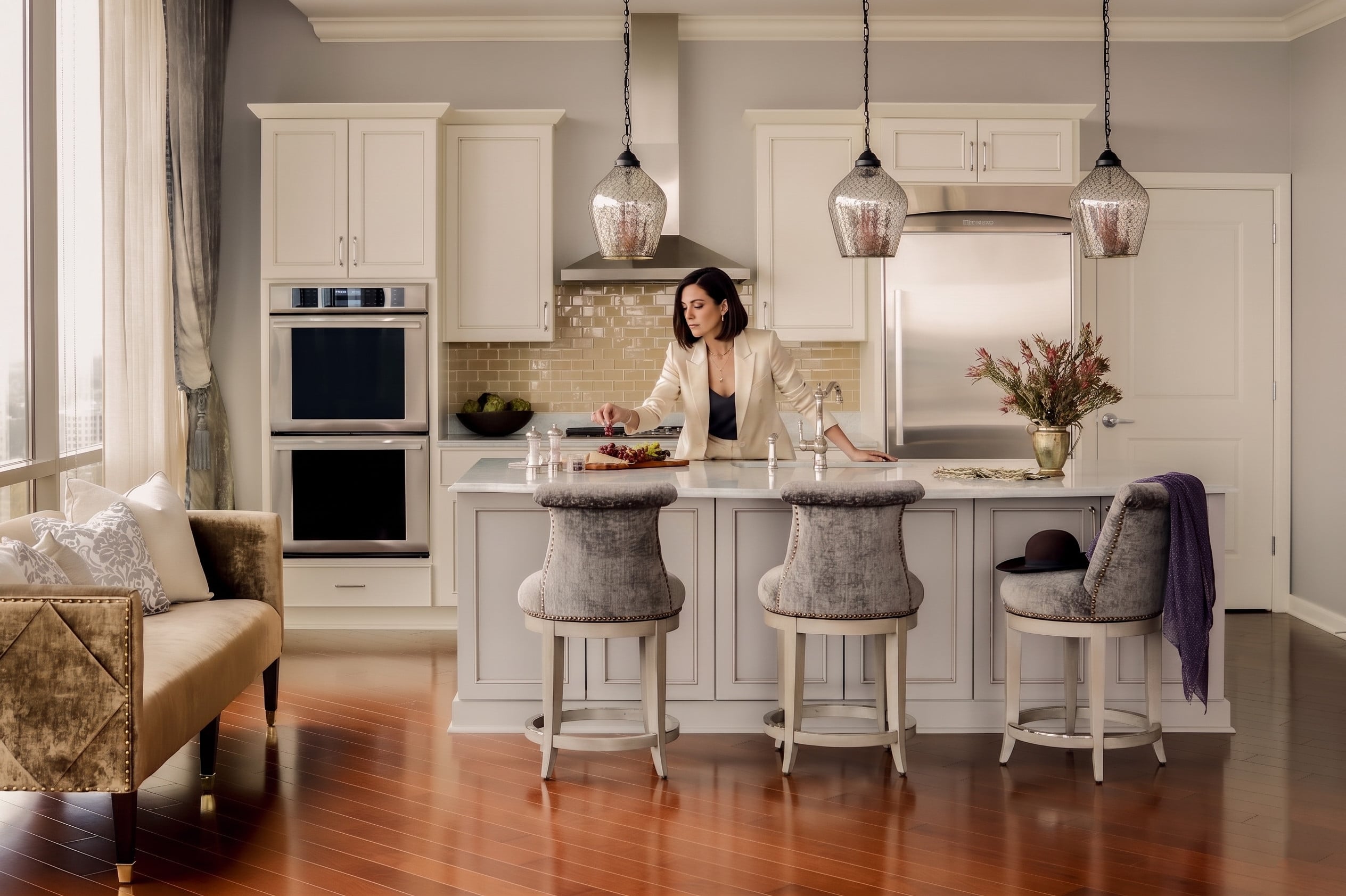 A woman in a cream blazer stands at a kitchen island, arranging grapes on a serving board.