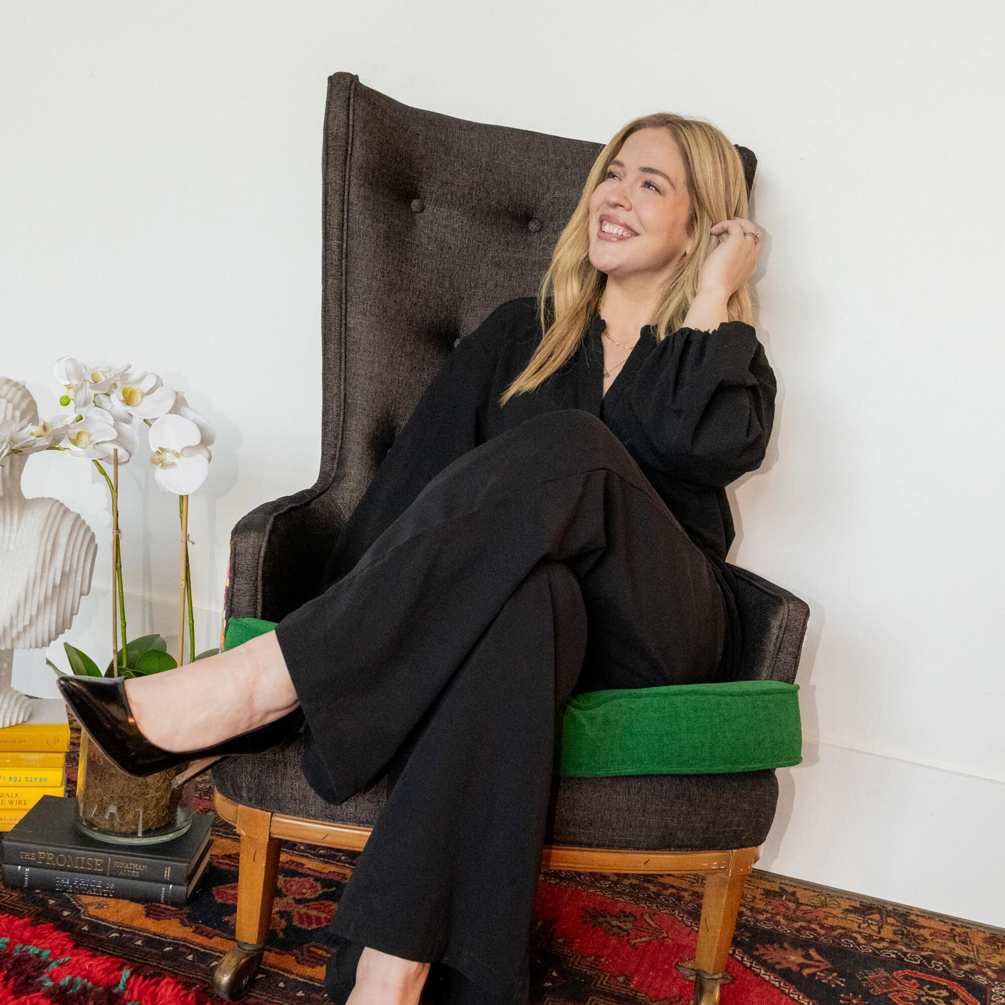 A smiling woman in a black outfit sits in a high-backed armchair.