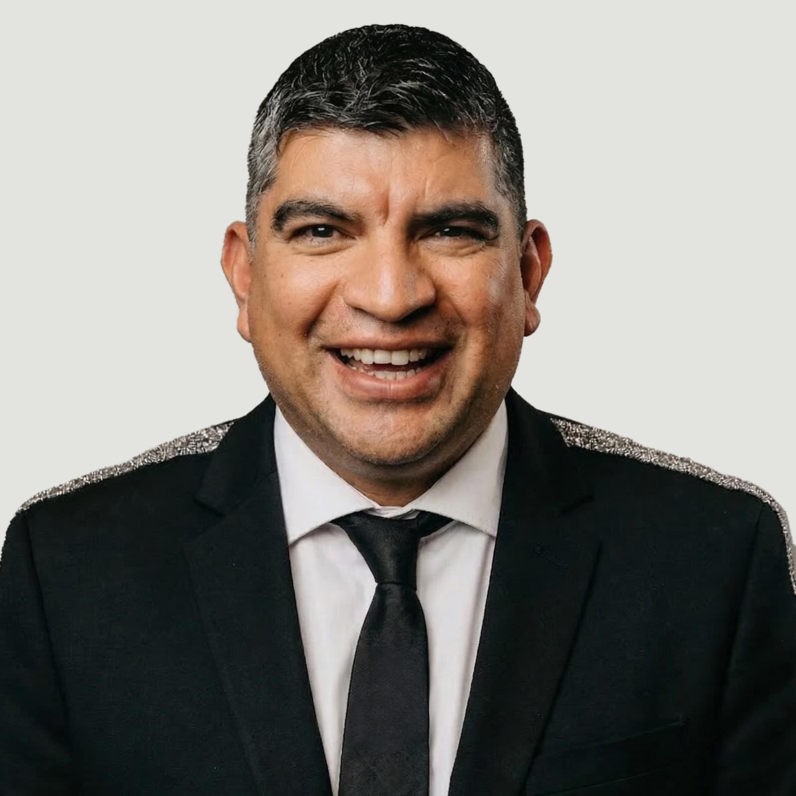 A portrait of a smiling man wearing a black suit, white shirt, and black tie.