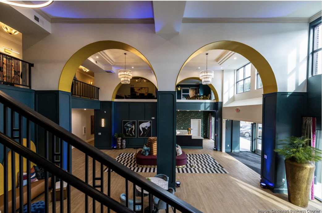 A modern lobby by Crimson Design Group with high ceilings, large arched doorways, lounge seating, decorative lighting, and a staircase in the foreground.