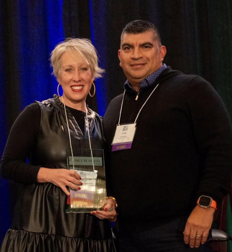 Two people from Crimson Design Group stand side by side at an event; the woman is holding a glass award and both are wearing conference name badges.