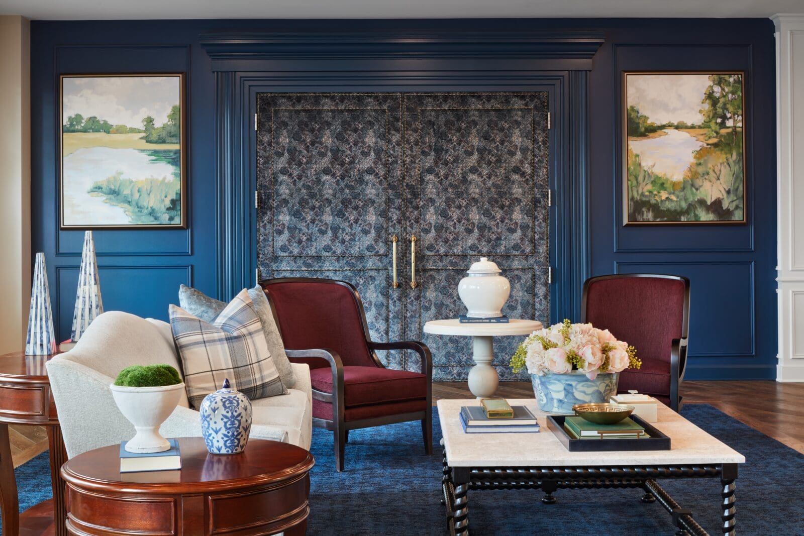 A sitting area with burgundy chairs, a cream sofa, decorative vases, wall art, and a blue patterned backdrop framed by blue paneling.