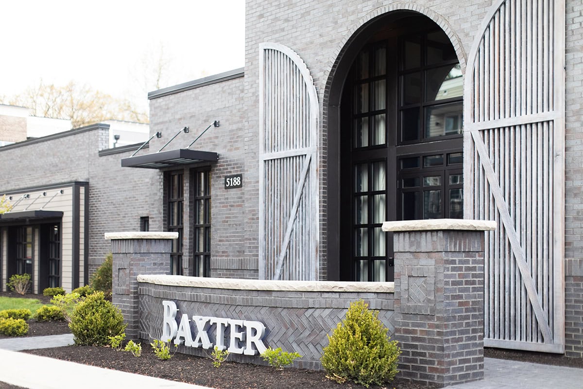 A modern brick building with large arched windows, metal gates, and a sign reading "Baxter" in front of the entrance.