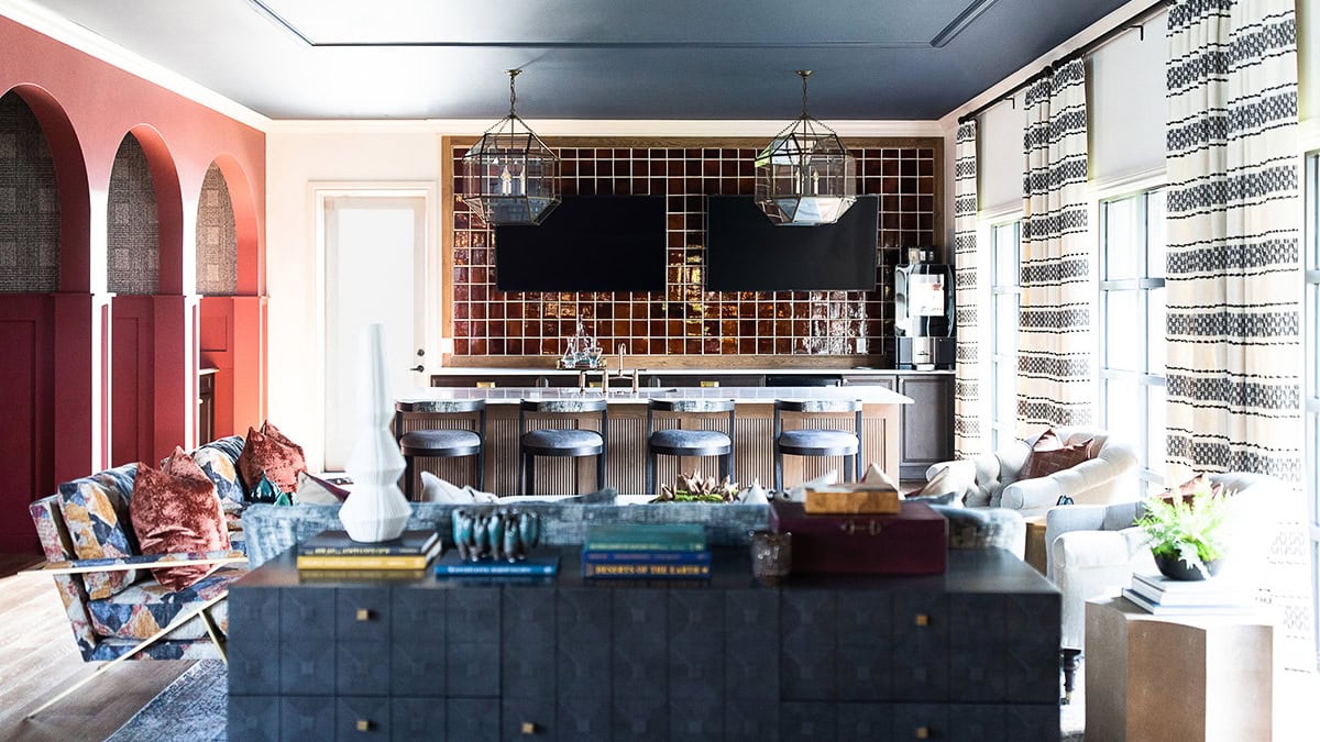 Modern living room and kitchen with a bar counter, four stools, two large pendant lights, patterned curtains, and eclectic seating arrangements.