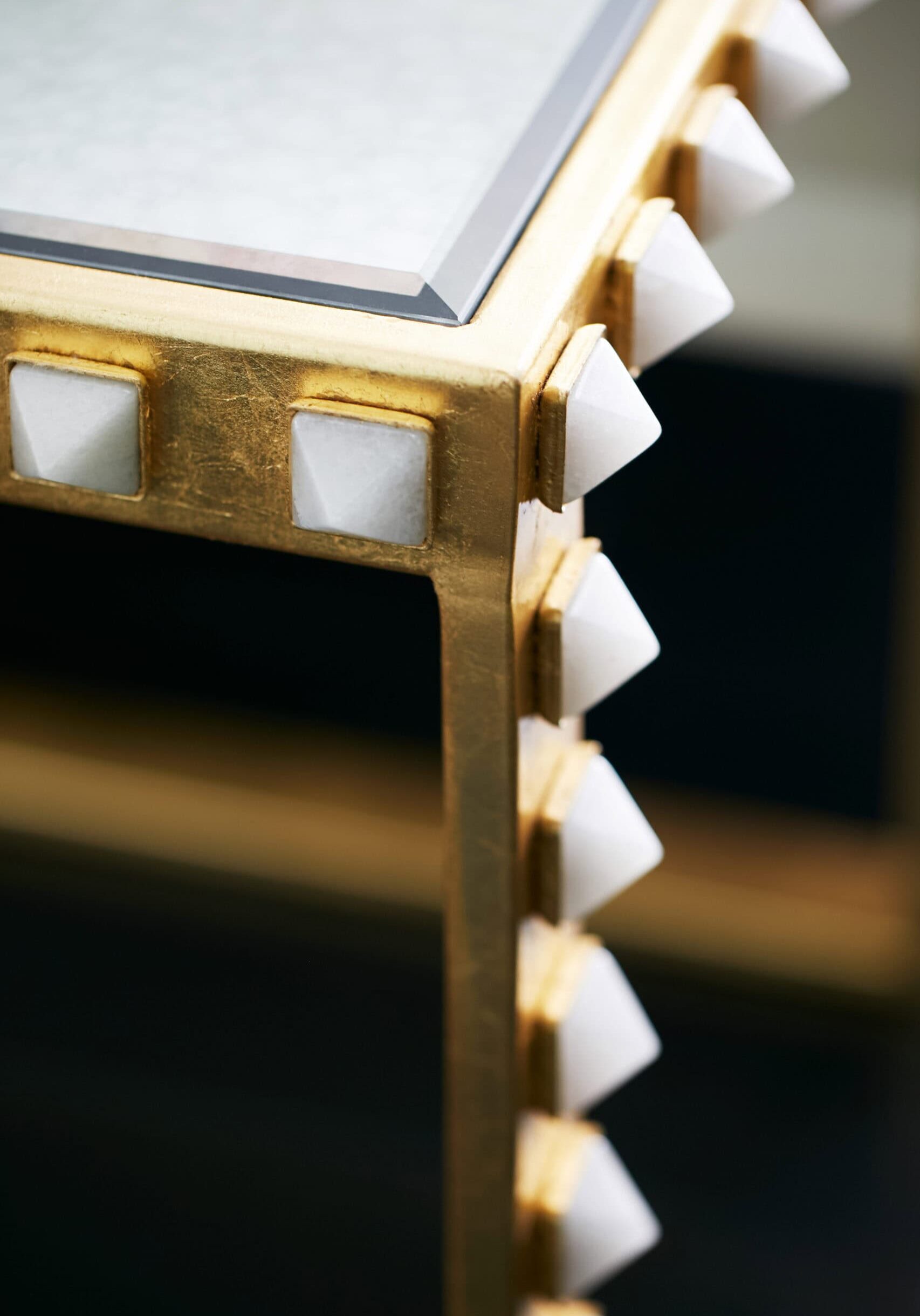 Close-up of a gold-colored table corner with a glass top and white pyramid-shaped studs along the edges.