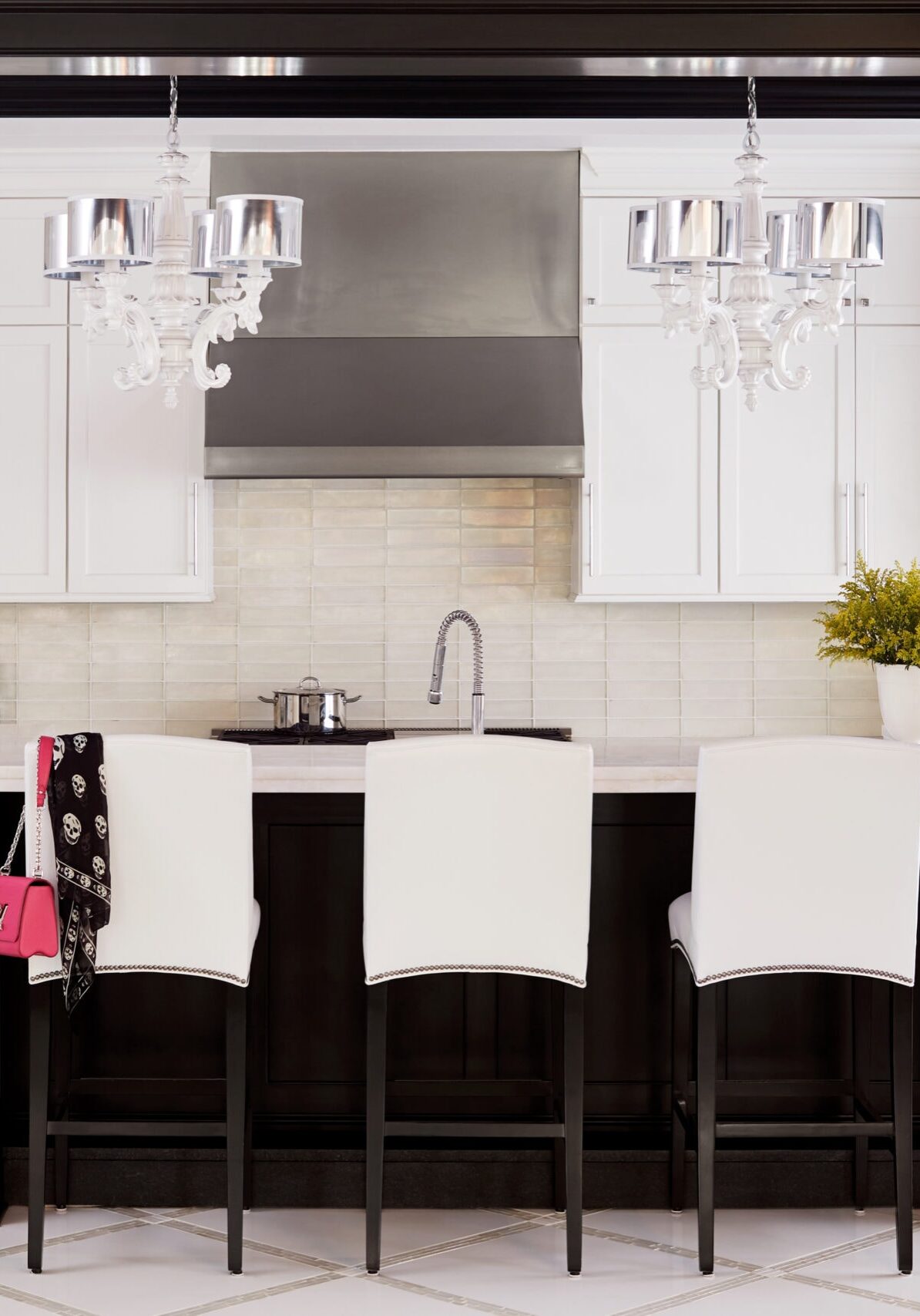 Modern kitchen with white cabinets, black island, three white chairs, stainless steel appliances, hanging chandeliers, and a vase with yellow flowers on the counter.