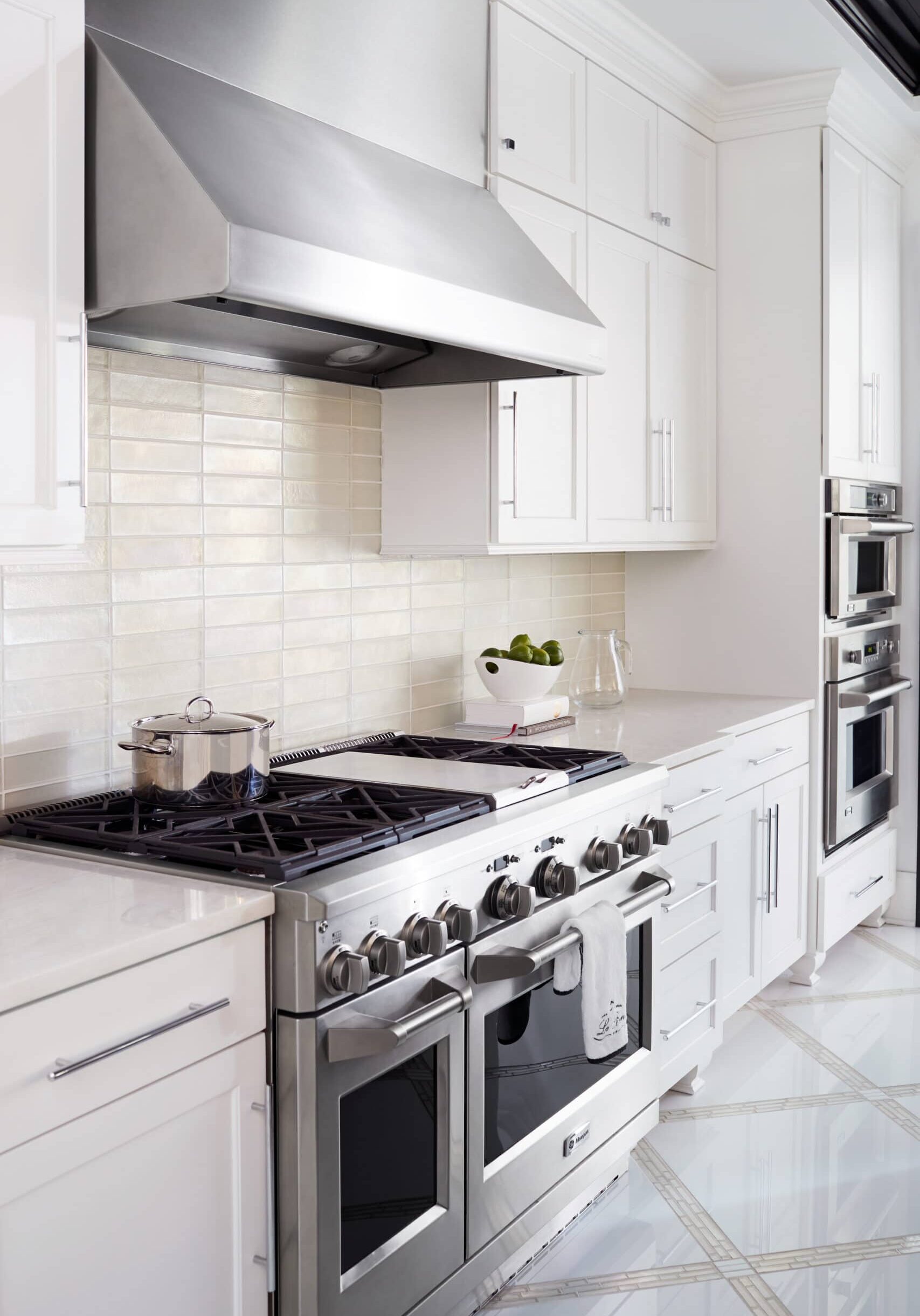 Modern kitchen with stainless steel stove and range hood, white cabinets, tiled backsplash, a pot on the stove, and a bowl of apples on the counter.