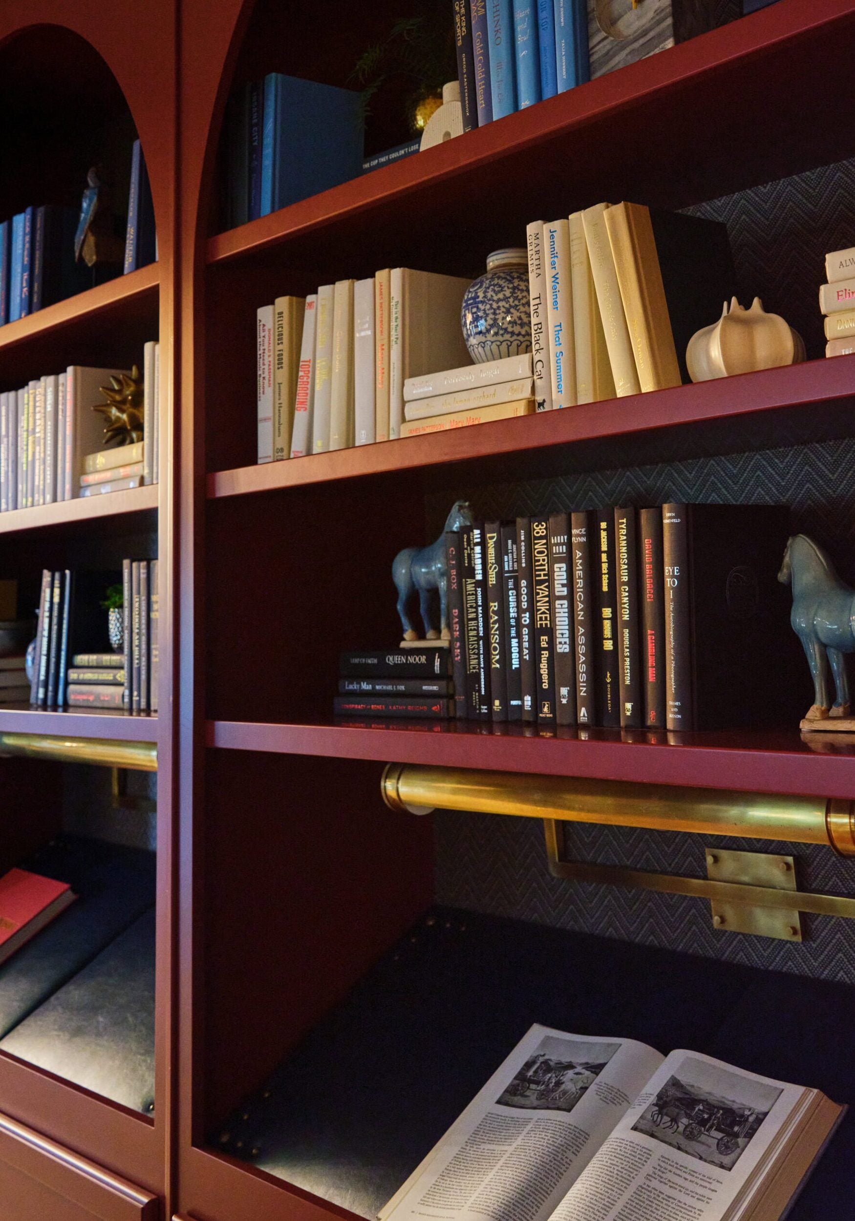 Bookshelves filled with assorted books, decorative items, two blue horse figurines, and an open book on a desk-lit surface below.