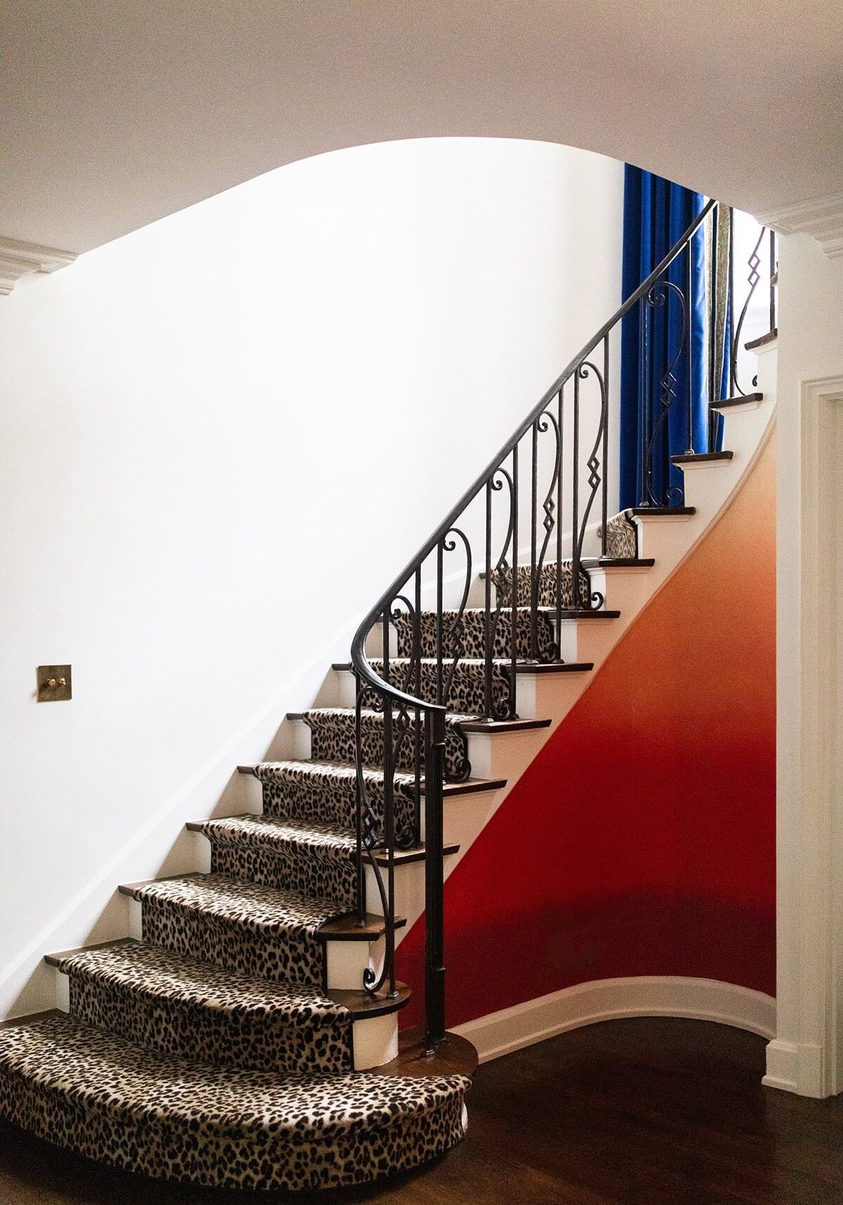 Curved staircase with leopard print carpet, black iron railing, white walls, and an orange accent wall.