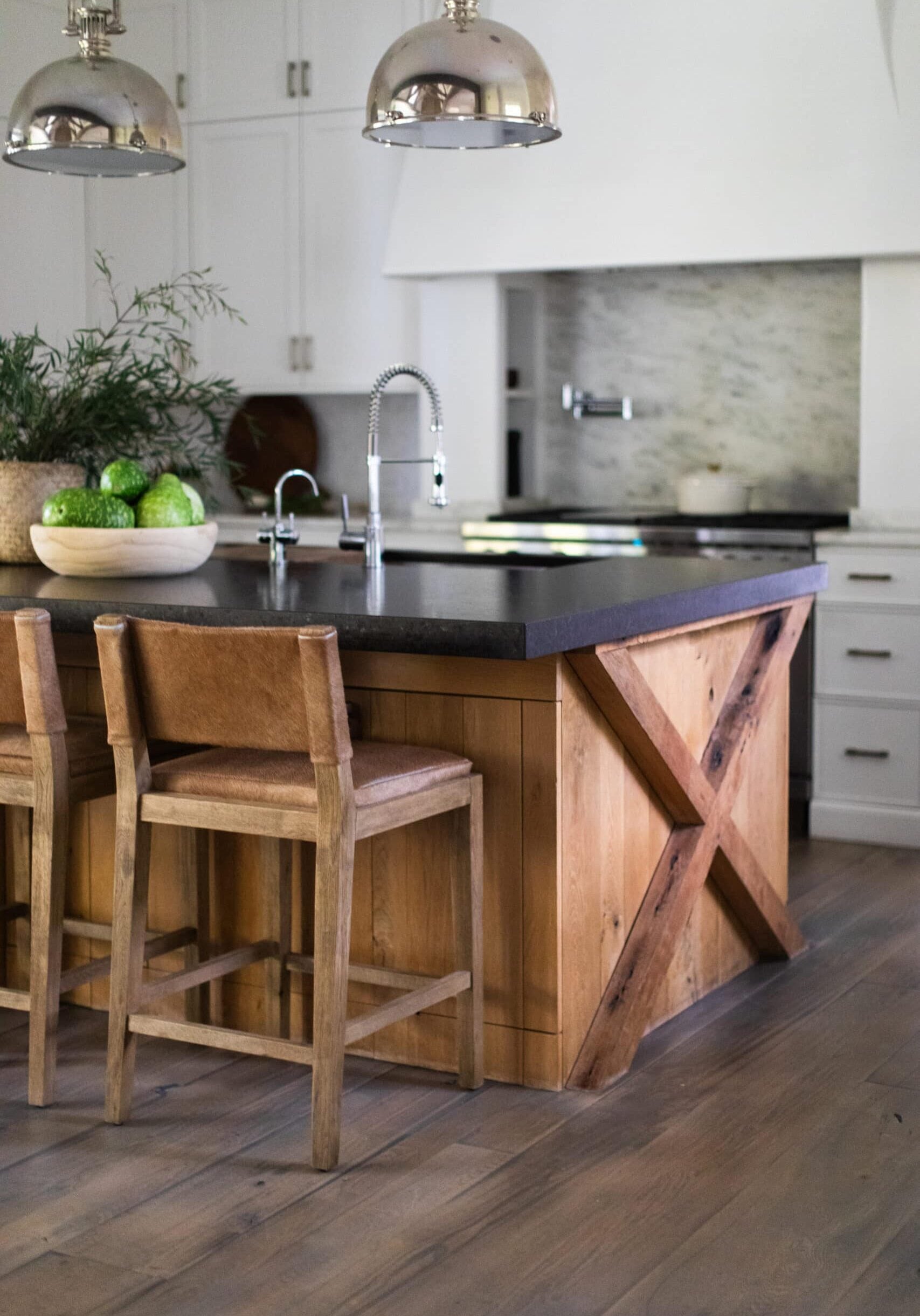 A modern kitchen with a wooden island, two wooden barstools, a black countertop, a sink with a gooseneck faucet, and two metallic pendant lights overhead.