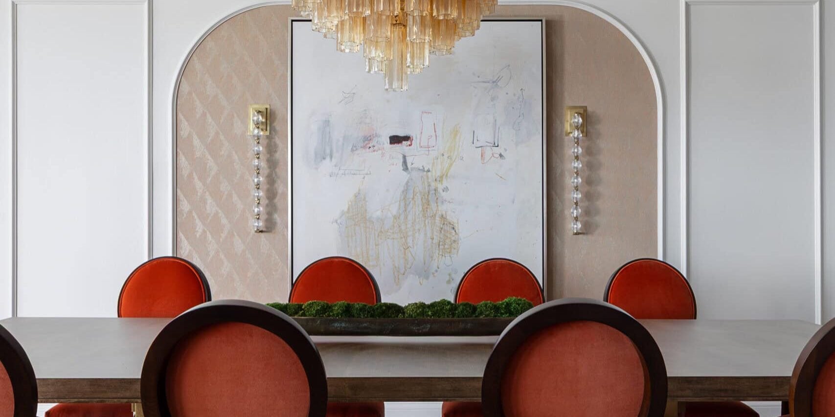 Elegant dining room with a rectangular table, red upholstered chairs, a gold chandelier, abstract wall art, and a patterned rug on a hardwood floor.