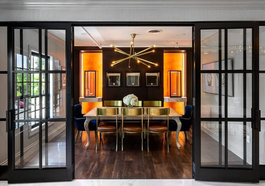 Modern dining room with gold chairs, a wooden table, a contemporary chandelier, and glass sliding doors; illuminated by warm, recessed wall lighting.