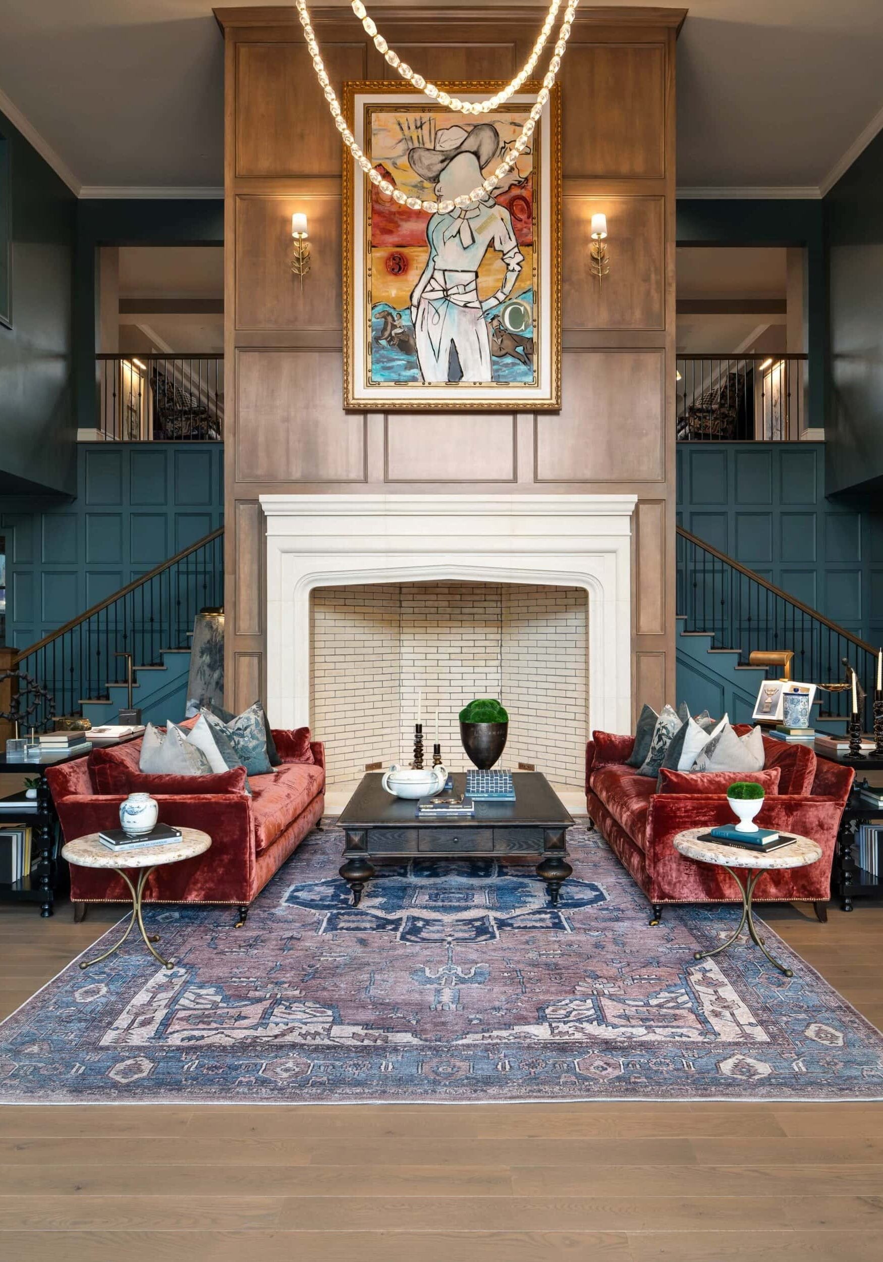 Elegant living room with two red velvet sofas, a large fireplace, contemporary art above the mantel, and a blue patterned rug on wooden floors—showcasing inspiration from Retail Design in Scottsdale, Arizona.