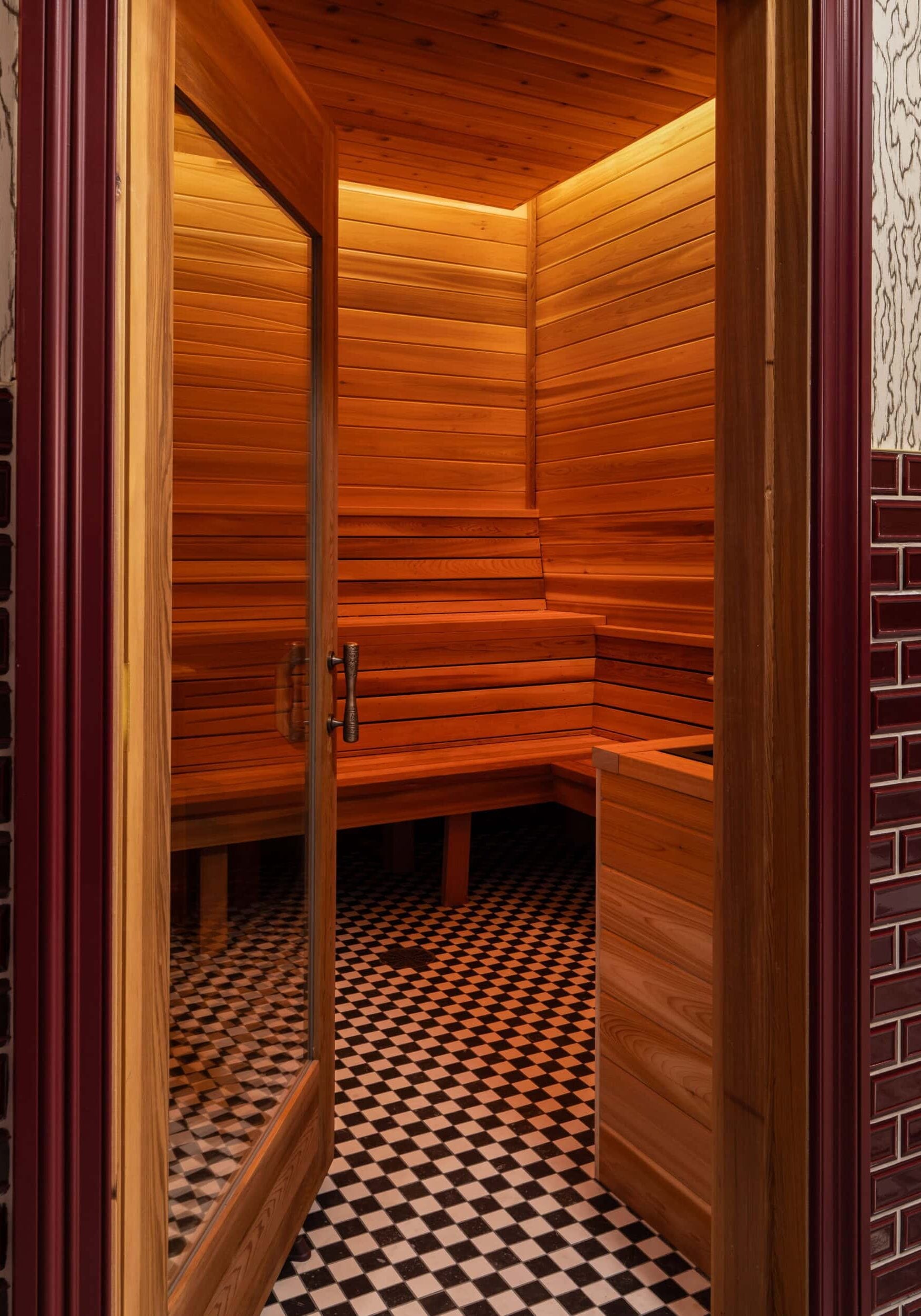 A wooden sauna room with bench seating, warm lighting, a glass door, and a black-and-white checkered tile floor showcases sophisticated retail design in Scottsdale, Arizona.