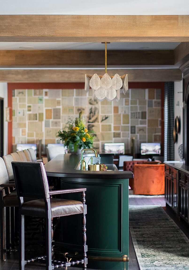 A modern, well-lit living space with a green bar, upholstered chairs, wood accents, a wall of art, and large windows allowing natural light inside.