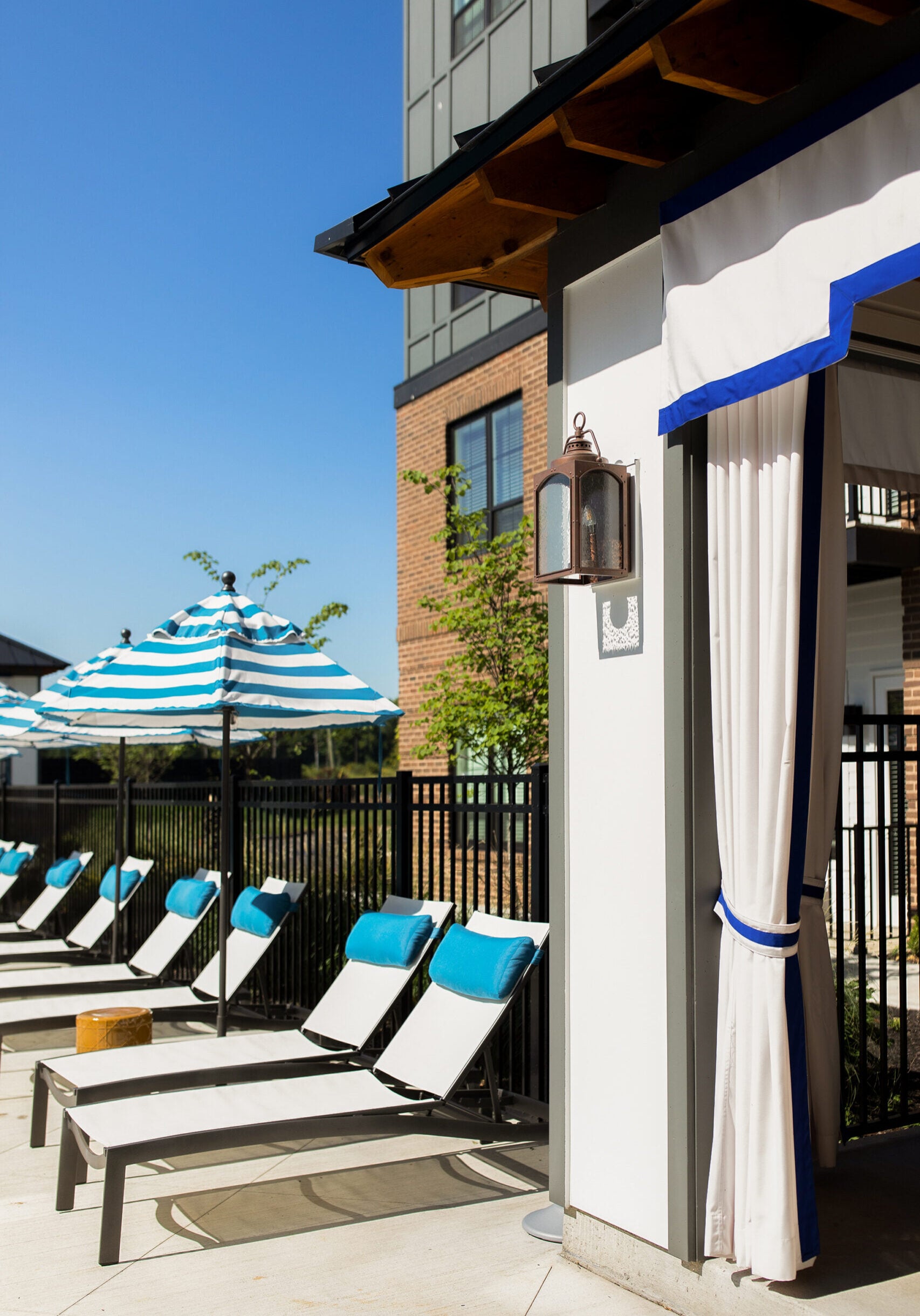 Lounge chairs with blue towels and striped umbrellas by a poolside cabana on a sunny day.