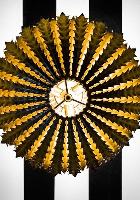 A luxury sunburst-style gold wall sconce mounted on a modern black and white striped architectural wall panel for a boutique commercial interior.