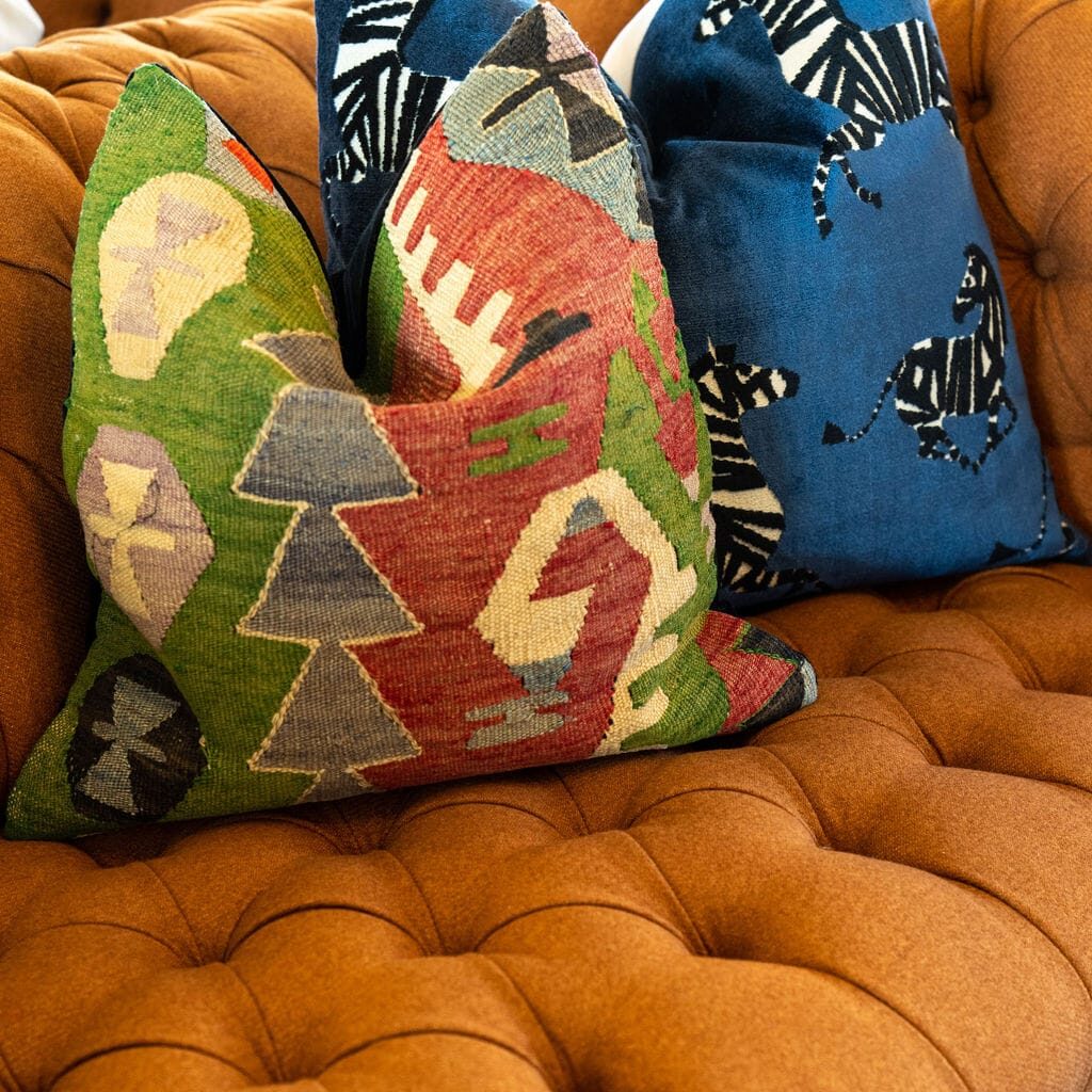 Two patterned throw pillows, one with a geometric design and the other with zebras, by Crimson Design Group, are placed on a tufted brown sofa.