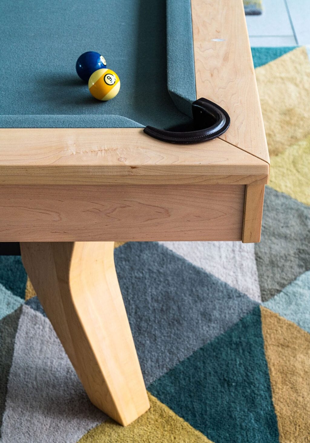 A close-up of a pool table corner with the 9-ball and 2-ball near a pocket, set on a geometric patterned rug.