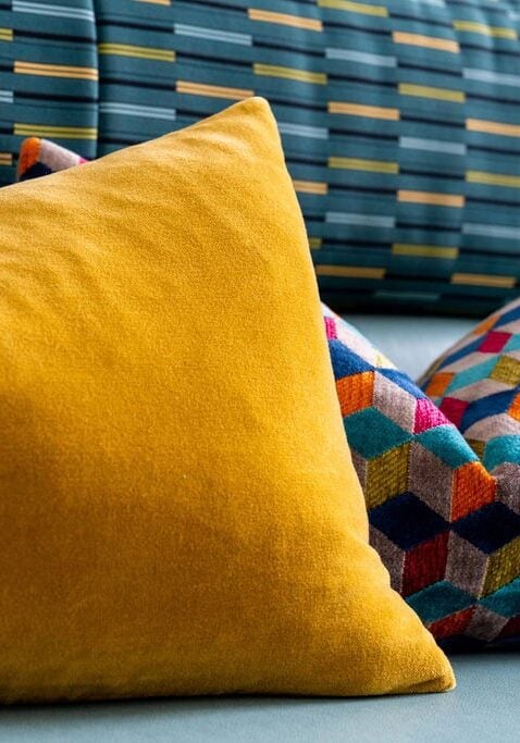A yellow pillow and a multicolored geometric-patterned pillow rest against a teal and yellow striped upholstered backrest.