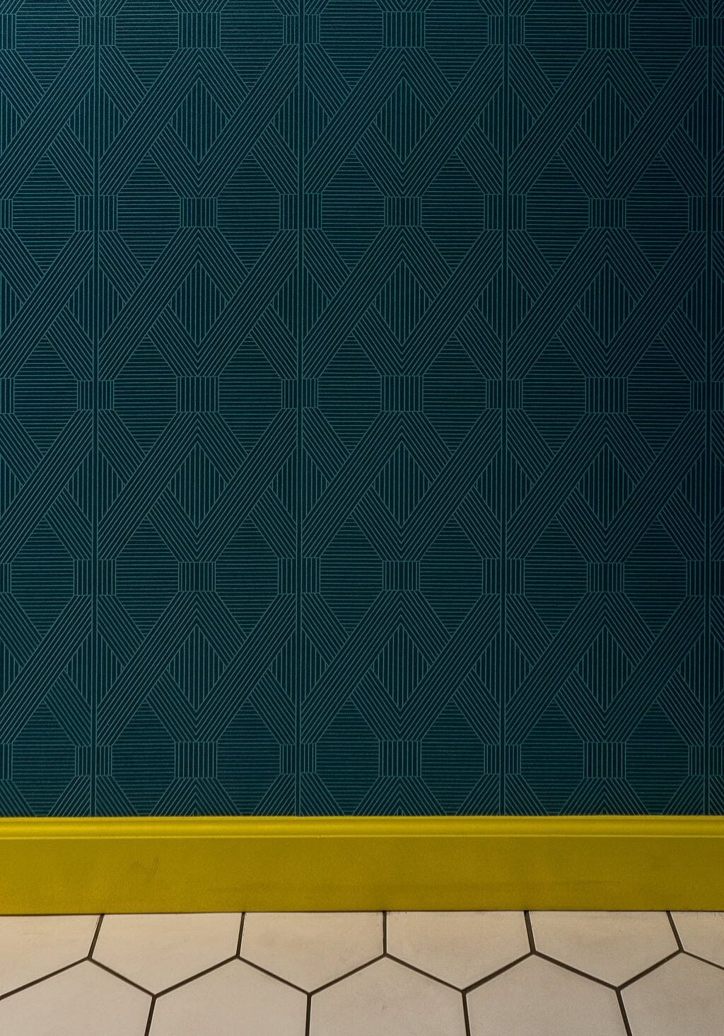 Dark teal geometric patterned wallpaper with a yellow baseboard and white hexagonal tile flooring.