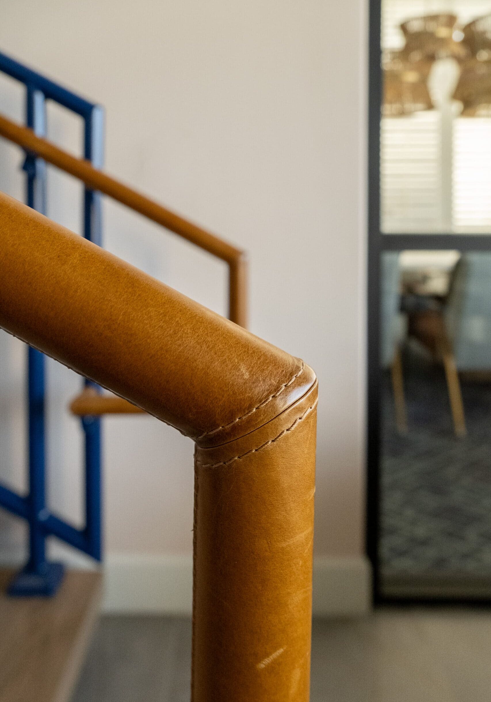 Close-up of a brown leather-wrapped handrail, with blue metal railings and part of a glass door in the background.