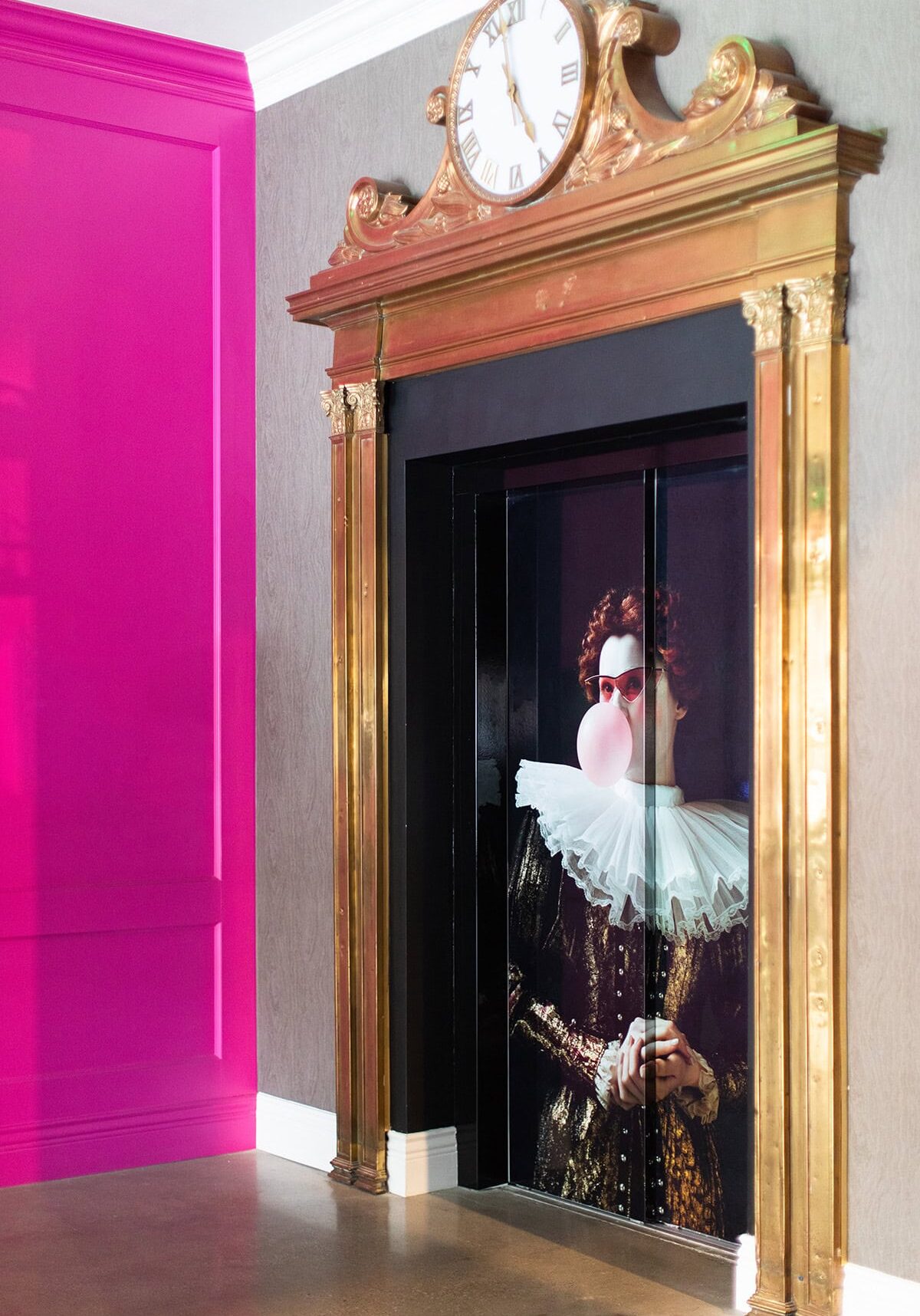 Elevator doors feature an image of a person in Elizabethan costume blowing bubblegum, set in a gold-frame elevator next to a bright pink wall.